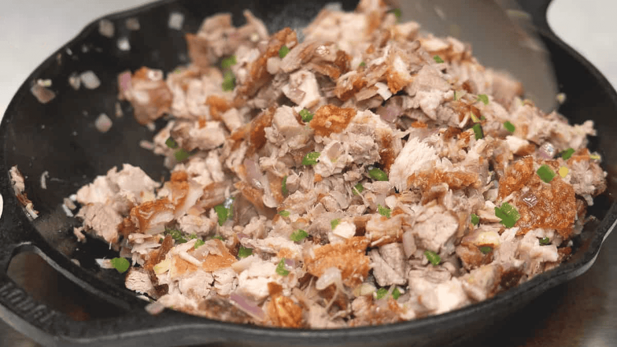 Mixing chopped pork belly and aromatics in a skillet.