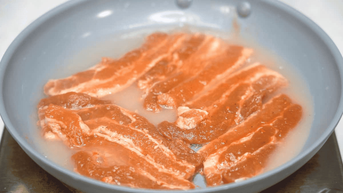 Marinated pork belly slices in some water in the skillet.