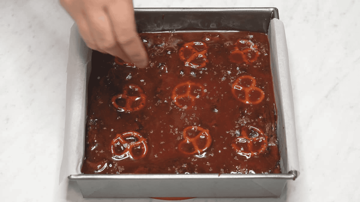 Sprinkling flaky salt on the salted caramel pretzel brownies in the pan. 