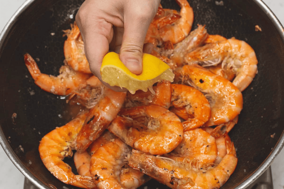 Squeezing half a lemon over the shrimp in the wok.
