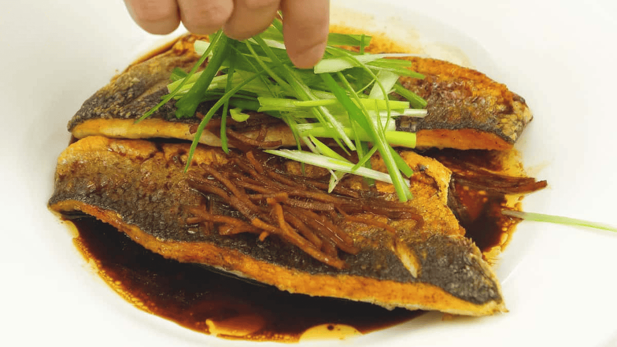 Adding scallions to the fish and sauce in the pan.