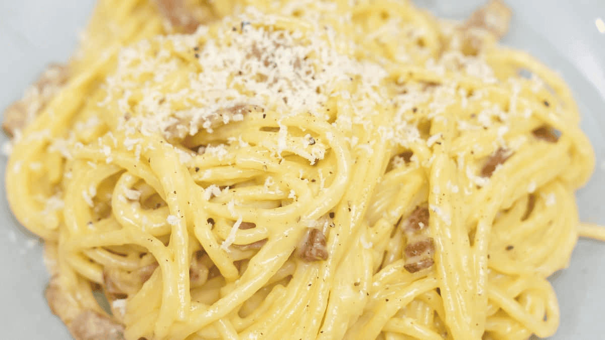 Spaghetti Carbonara on a plate with more cheese and black pepper on top.