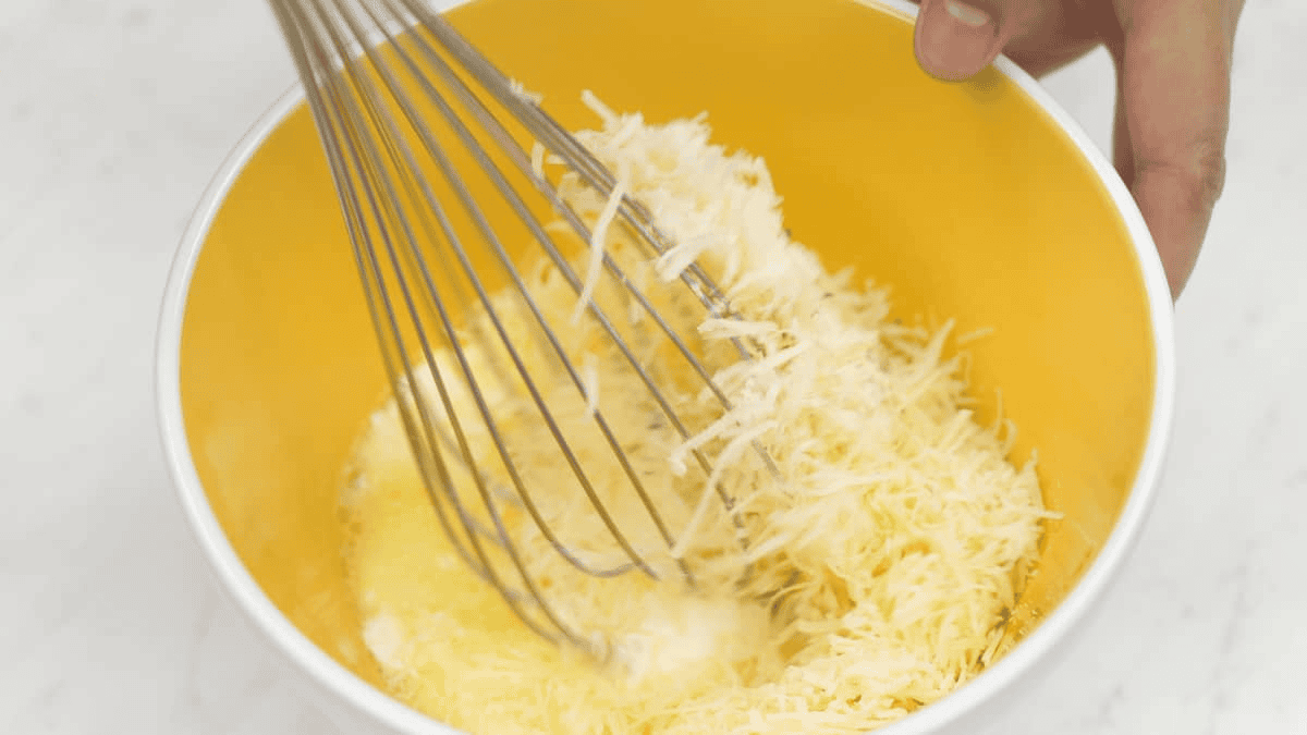 Whisking eggs, cream, and cheese together in a bowl.