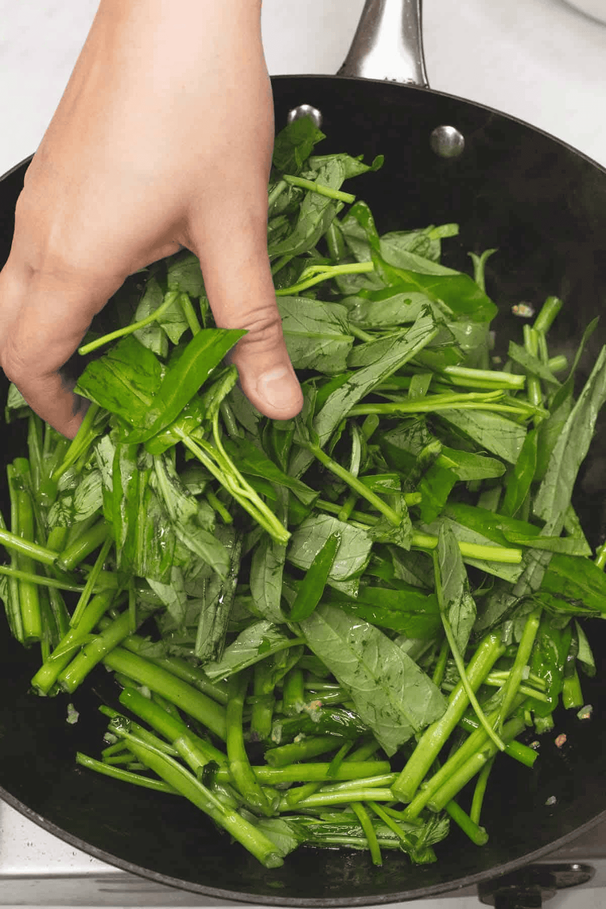 Adding the kangkong leaves to the wok.