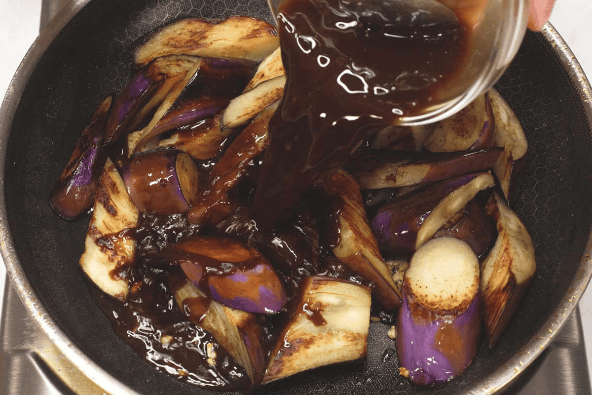 Adding sauce to the seard eggplant in the skillet.