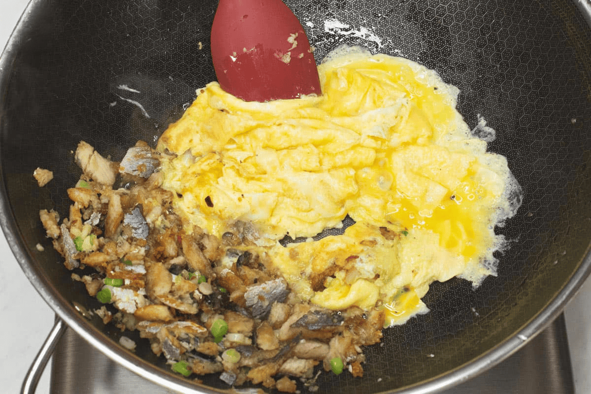 Cooking the eggs in a wok, with tinapa flakes and aromatics on the side.