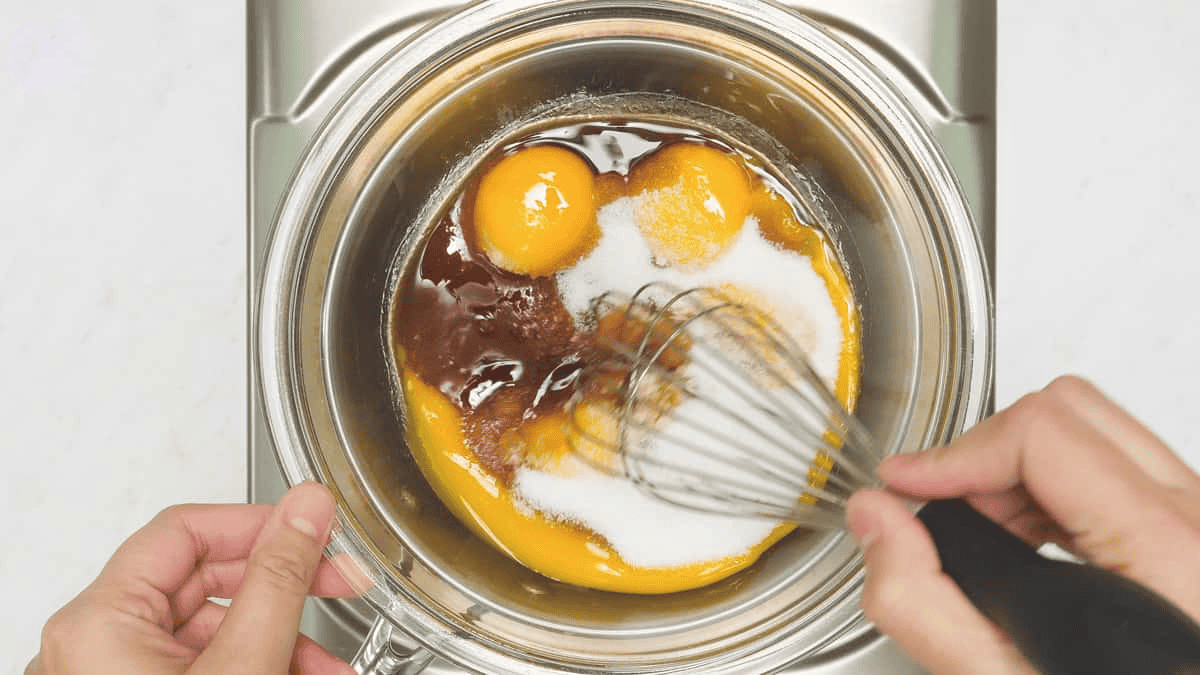 Whisking the egg yolk mixture in the bowl over the saucepan.