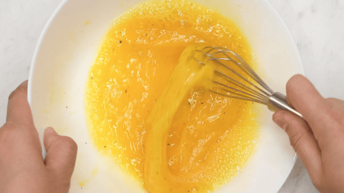 Beating the eggs in a bowl using a whisk.