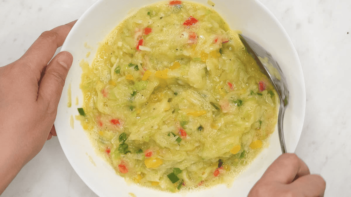 Combining the eggs with grated chayote and sauteed aromatics.