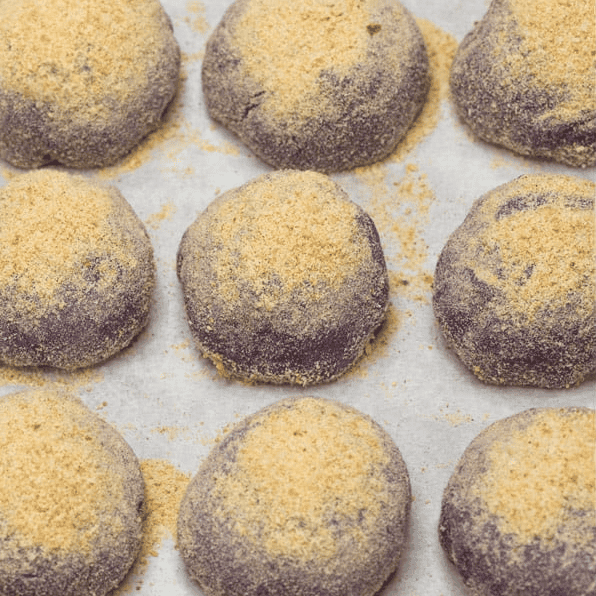 Shaped ube pandesal coated in breadcrumbs on a baking sheet.