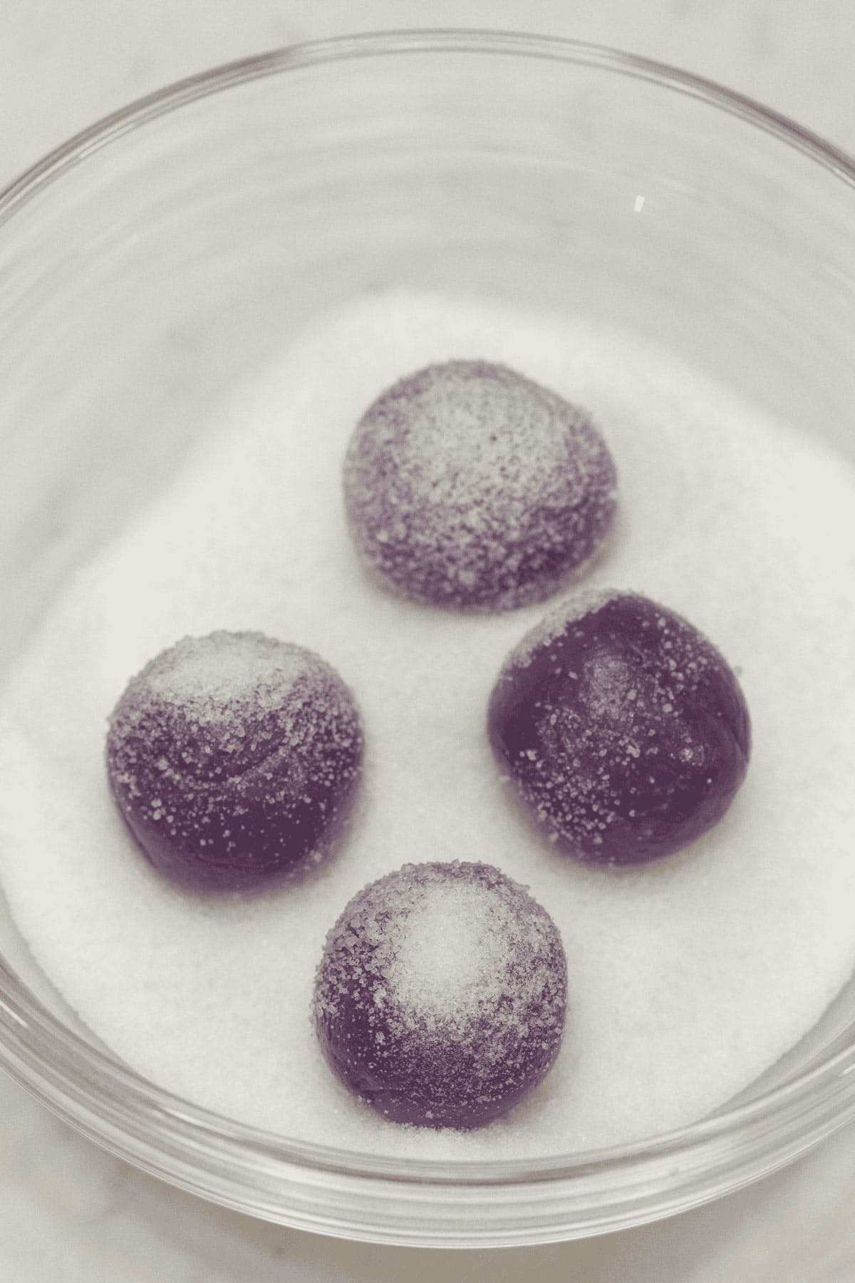 Coating the Ube Pastillas with granulated sugar in a bowl.