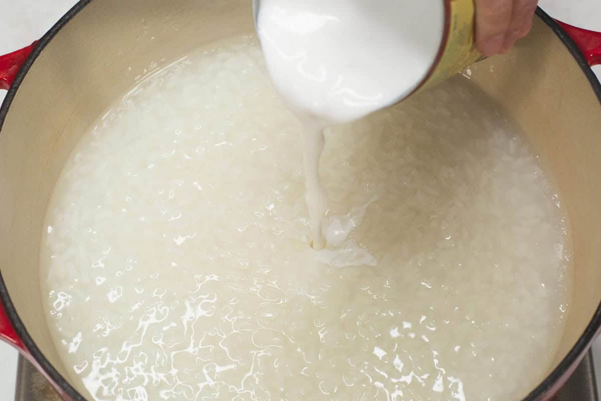 Adding coconut milk to the rice mixture in the pot.