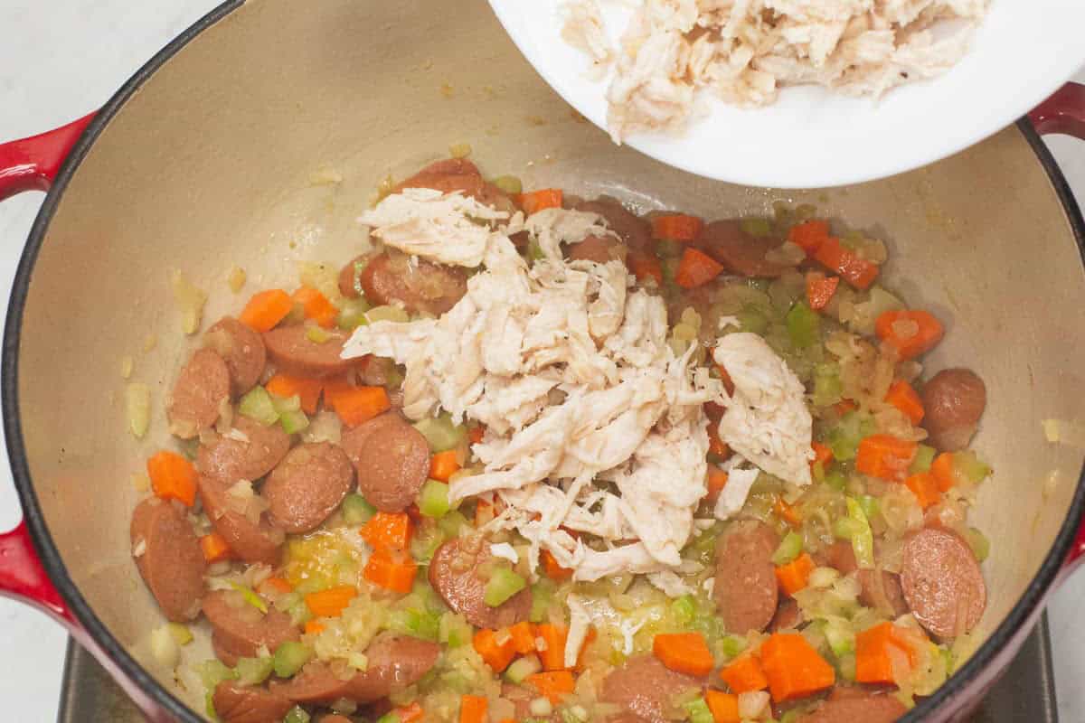Adding the shredded chicken to the aromatics, vegetables, and hotdogs in the pot.