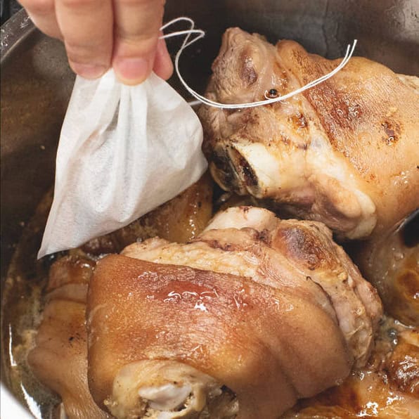 Adding the spices in a mesh bag to the mixture in the pot.