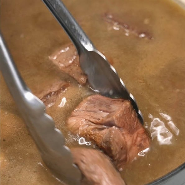 Skimming off the fat and foam on the surface. Adding pieces of beef chuck into the mixture.