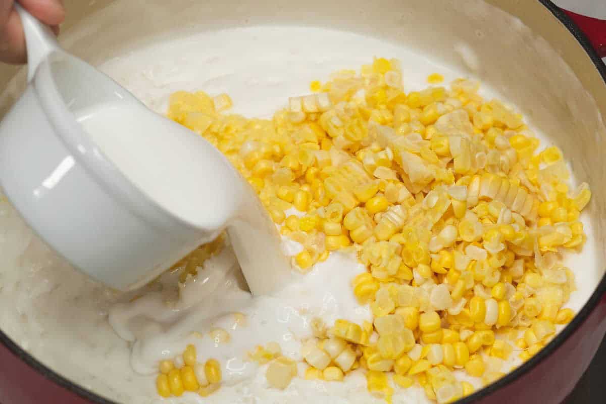 Adding coconut cream to the corn and coconut milk mixture in the Dutch oven.