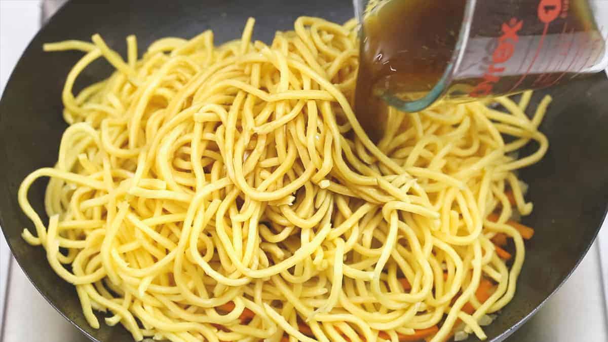 Pouring the sauce to the noodles in the wok.