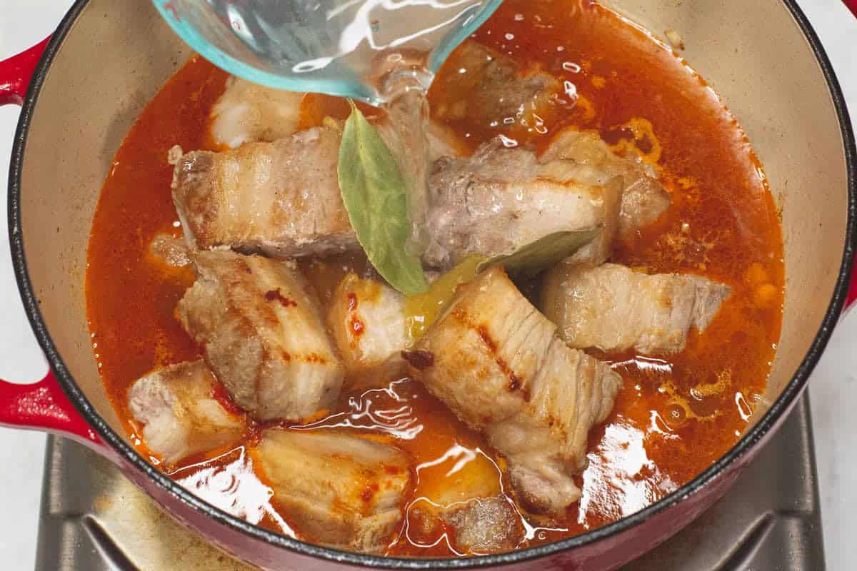 Adding water to the meat and other ingredients in the pot.