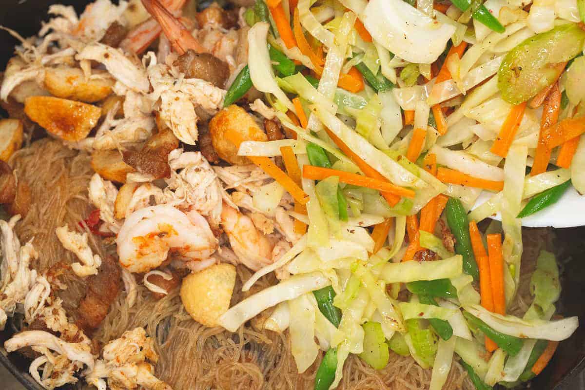 Adding the proteins and vegetables to the noodles in the wok.