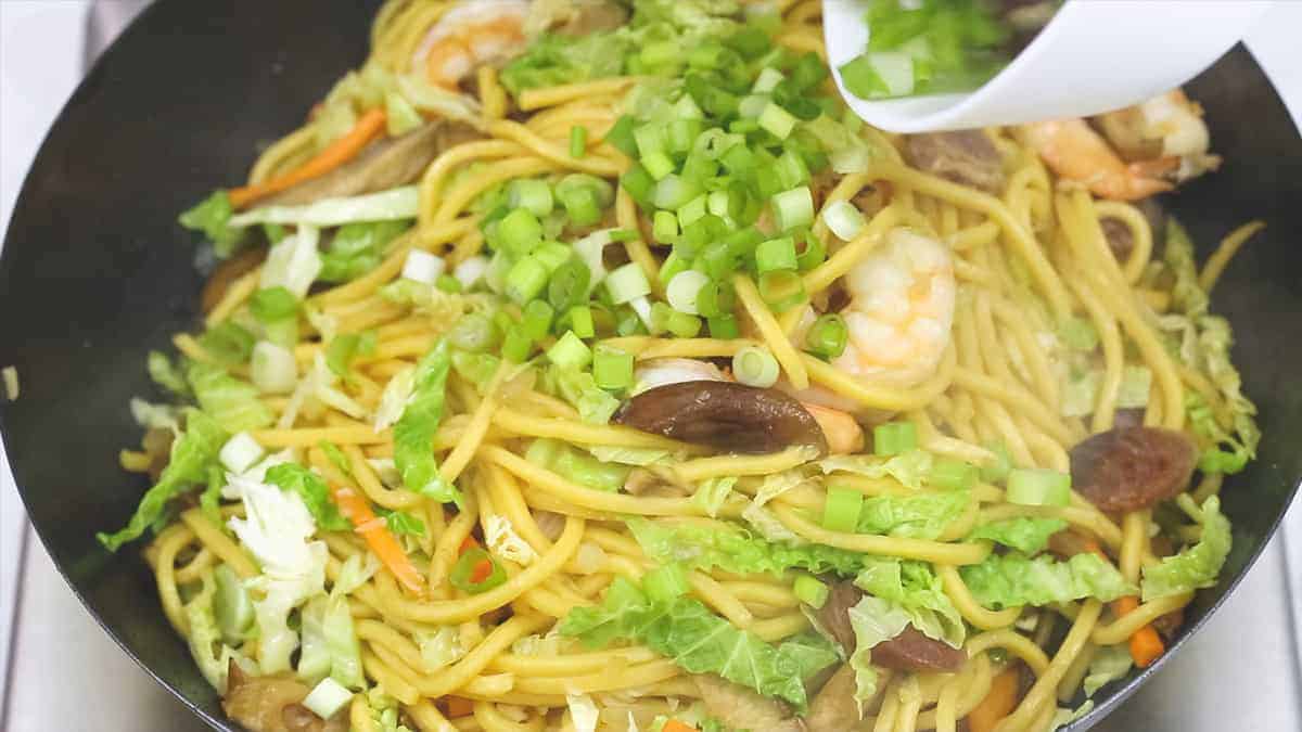Adding scallions to the Pancit Canton in the wok.