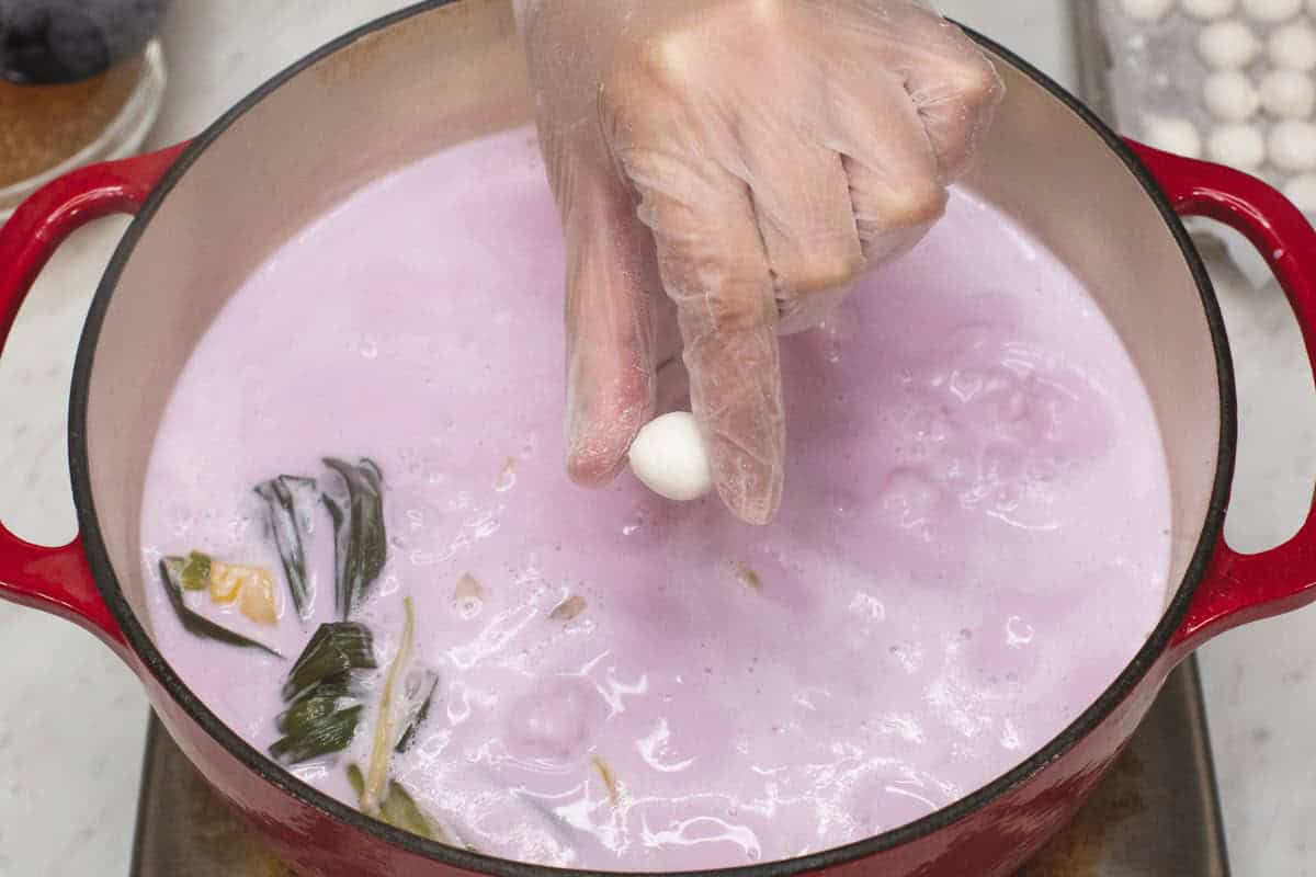 Dropping the glutinous rice balls one at a time into the boiling mixture.