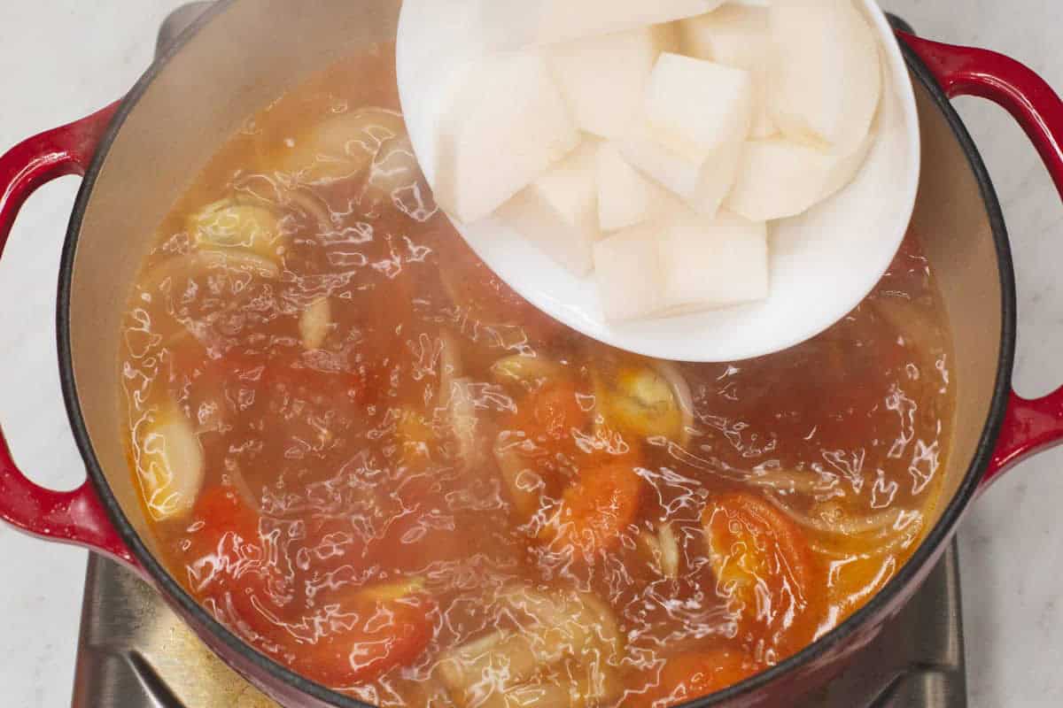 Adding radish to the boiling mixture in the pot.