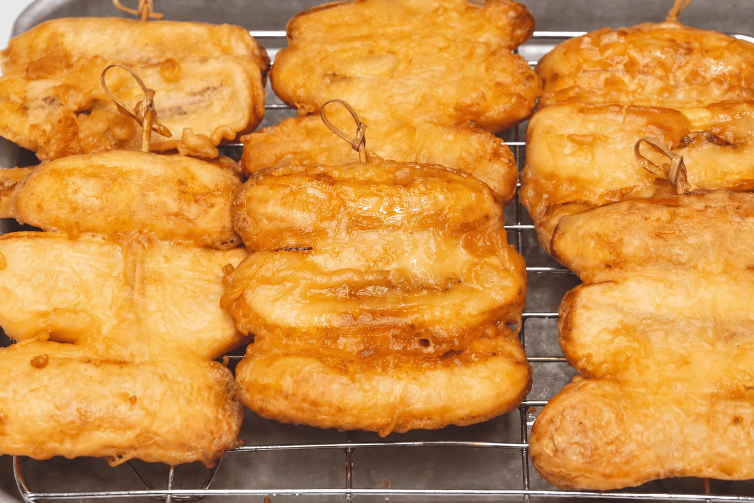 Draining fried saba bananas on a wire rack.