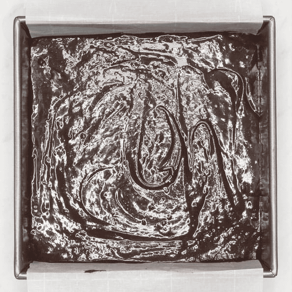 Brownie batter spread in a parchment-lined baking pan.