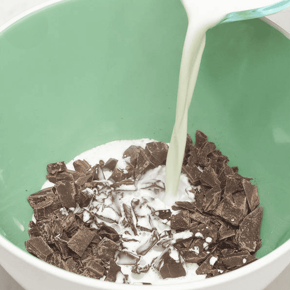 Pouring hot cream over chopped chocolate in a green bowl.