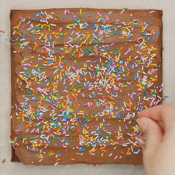 Adding colorful sprinkles to ganache-frosted brownies.