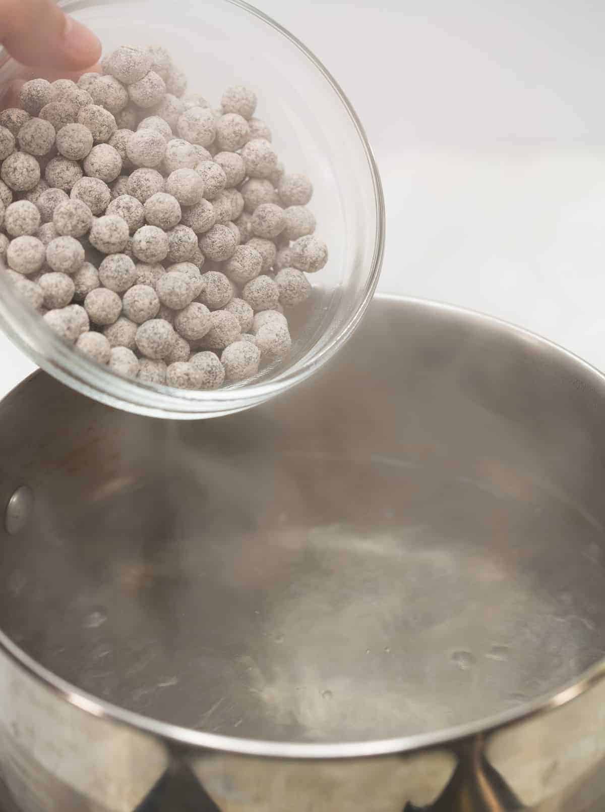 Adding raw tapioca pearls to the boiling water in the saucepan.