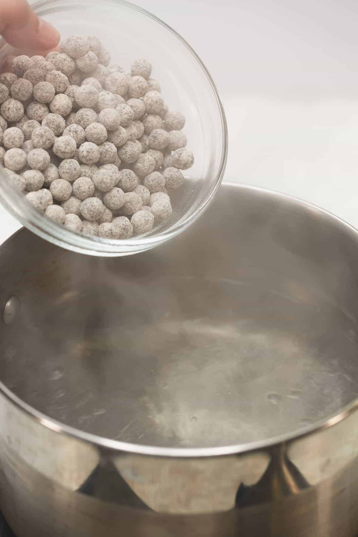 Adding raw tapioca pearls to the boiling water in the saucepan.
