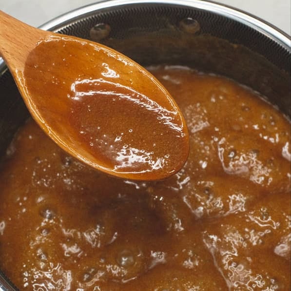 Latik sauce on a wooden spoon and dropping a small amount on a parchment paper.