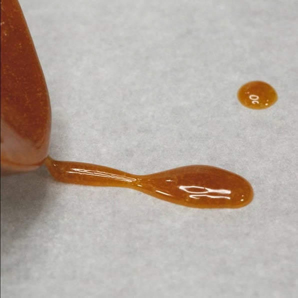 Latik sauce on a wooden spoon and dropping a small amount on a parchment paper.