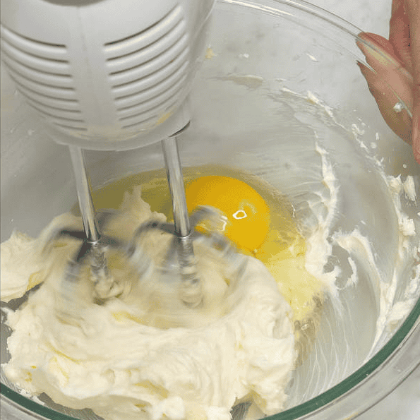 Beating an egg into the cream cheese mixture.