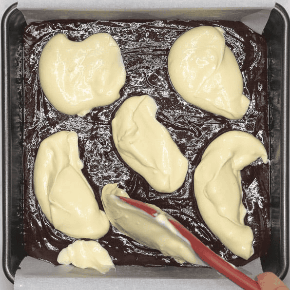 Adding dollops of cheesecake batter over brownie batter.