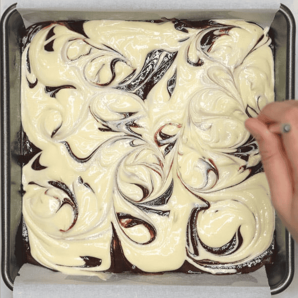 Swirling cheesecake and brownie batter with a chopstick.