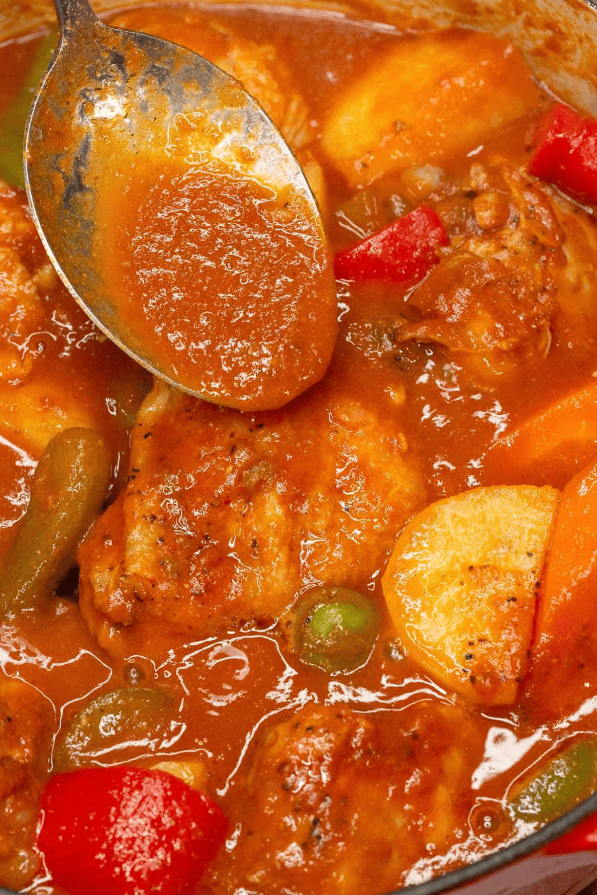 Sauce on a spoon from the pot filled with Chicken Caldereta.