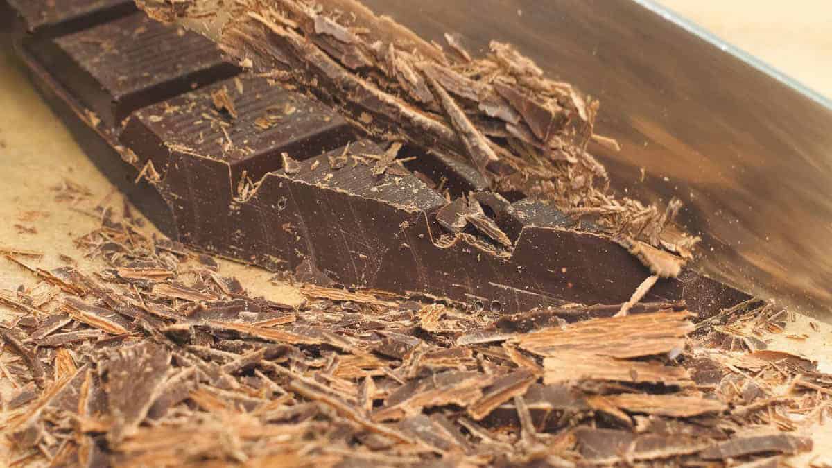 Making chocolate shavings using a knife on a parchment paper-lined board.