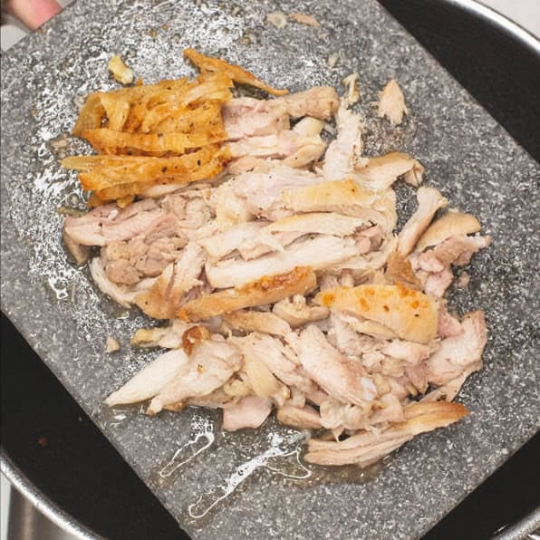 Searing the chicken in a wok, then shredding it on a cutting board.