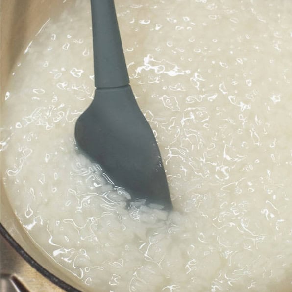 Adding water to the glutinous rice in the pot. Mixing the simmered glutinous rice in the pot.
