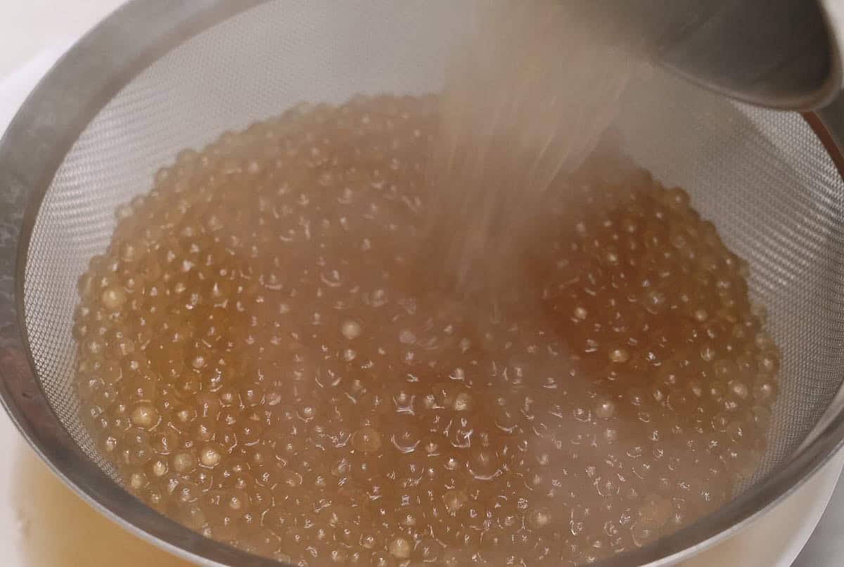 Draining the sago pearls using a strainer over a bowl.