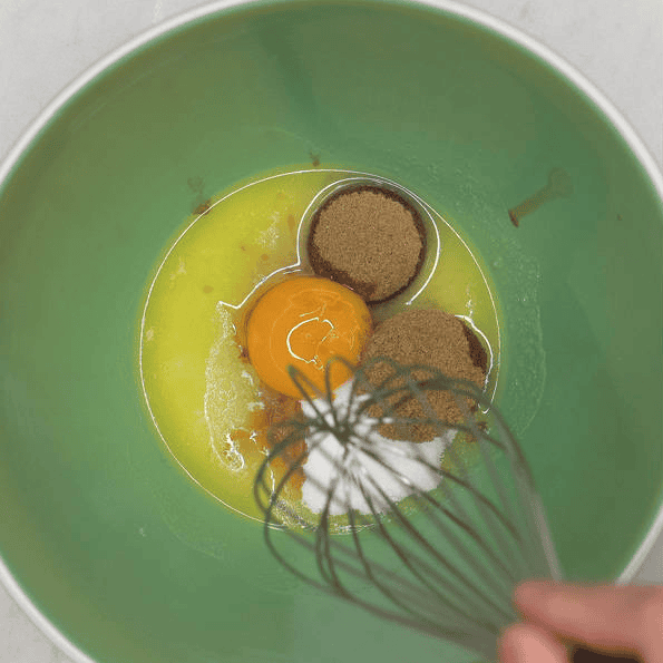 Whisking butter, sugars and egg in a green bowl.
