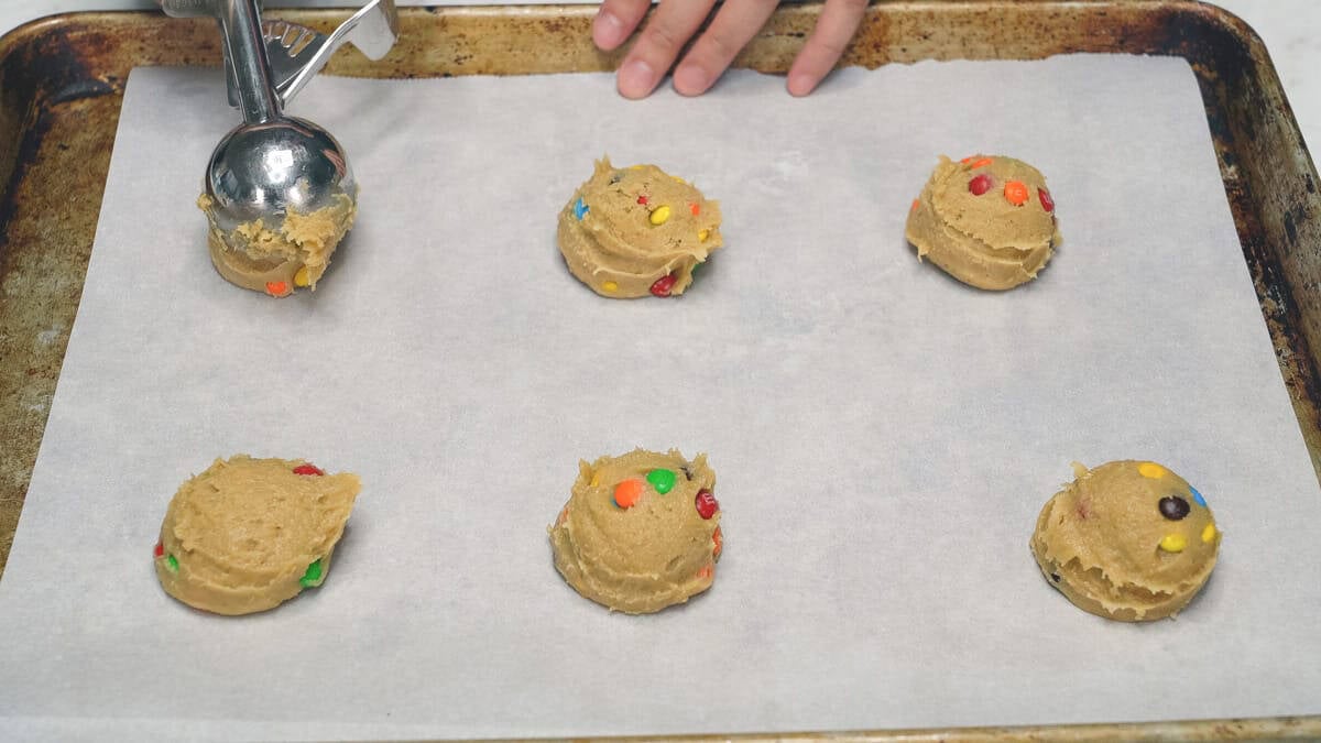 Arranging cookie dough balls on a parchment paper-lined baking sheet.
