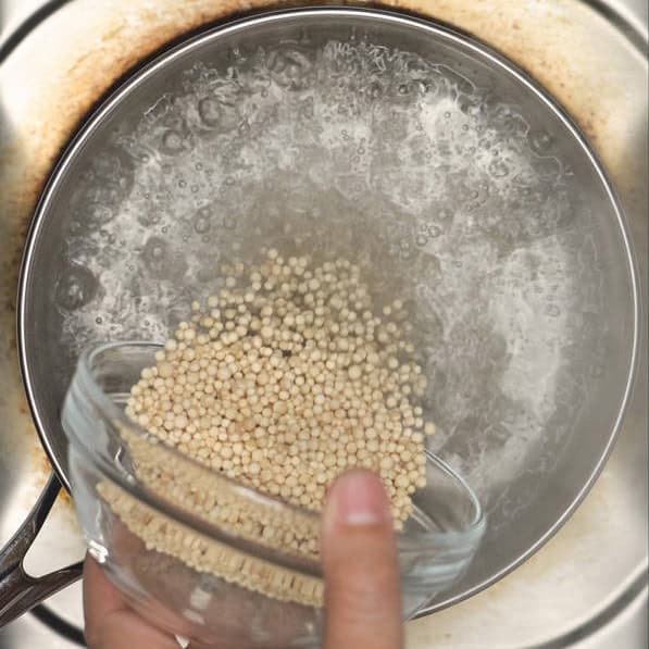 Adding the sago into the boiling water. Stirring the sago in the water using a slotted spoon.