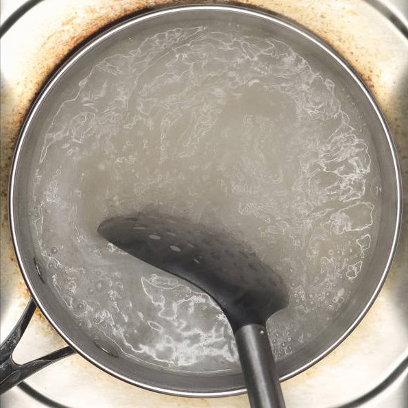Adding the sago into the boiling water. Stirring the sago in the water using a slotted spoon.