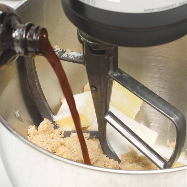 Adding vanilla extract to the butter and sugar in the bowl of the stand mixer. Scraping the sides of the bowl with a spatula.