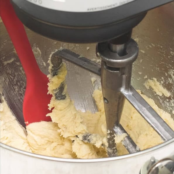 Adding vanilla extract to the butter and sugar in the bowl of the stand mixer. Scraping the sides of the bowl with a spatula.