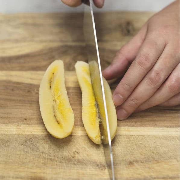 Slicing the saba banana and jackfruit lengthwise on a cutting board.