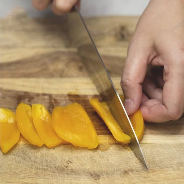 Slicing the saba banana and jackfruit lengthwise on a cutting board.
